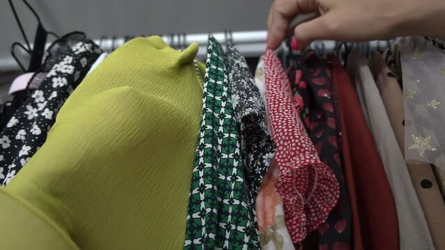 Young woman with pink manicure sorts out elegant clothes hanging on rack in wardrobe thinking what to wear close low angle shot