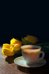 A cup of black tea flowing in cup against yellow flowers and black background