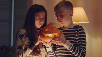 Obraz na płótnie Canvas Boy and girl playing with carved pumpkin at home on Halloween,