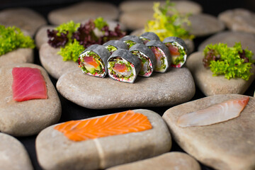Macro shot of Japanese sushi roll without rice with raw fish wrapped in daikon radish served on sea stones. Salmon, tuna, haddock fillets and salad mix on stones near no rice dish
