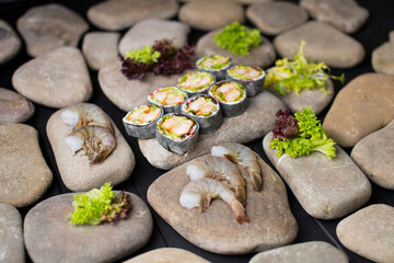 Close up of Japanese sushi roll without rice with tempura shrimp wrapped in daikon radish served on sea stones. ingredients on background. raw black tiger shrimps and salad mix near keto no rice dish
