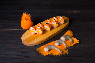 Side view of Japanese sushi roll without rice wrapped in carrot slices served on wooden plate. Cooking ingredients on dark background. raw black tiger shrimps on Carrot slices near Keto no rice dish
