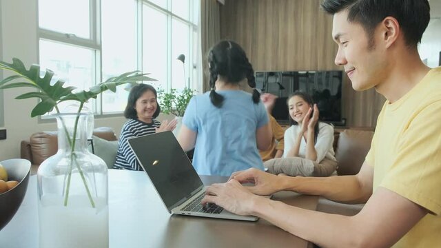 Young Asian father use laptop work at home with big family mom ,daughter ,grandfather grandmother ,palying fun laugh smile sit on sofa couch together in living room