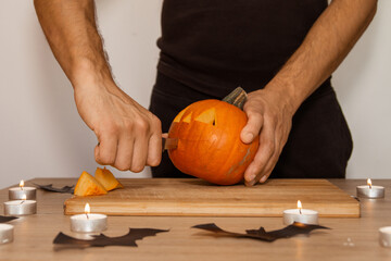 A man carves eyes and a mouth in a pumpkin for Halloween.