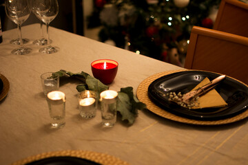 A lit red candle that illuminates a beautiful table, decorated and prepared for Christmas dinner.