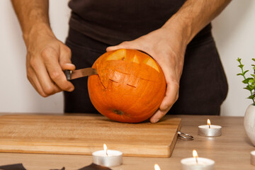 A man carves eyes and a mouth in a pumpkin for Halloween.