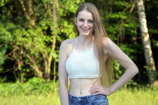 Sch&ouml;ne junge Frau tr&auml;gt Hot Pants und Oberteil bauchfrei und lacht an einem sonnigen Sommertag im Park