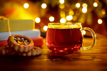 Hot tea in a glass transparent cup on wooden board with light bokeh in a background. Warm christmas...