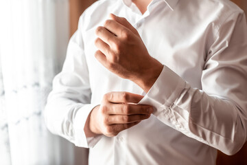 Grooms morning preparation, handsome groom getting dressed and preparing for the wedding, white shirt. Groom morning preparation. Young groom getting dressed in a wedding shirt
