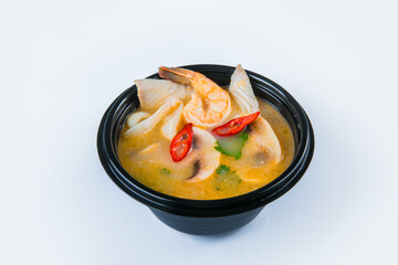 Asian spicy Tom Yam soup with black tiger shrimp, calamari, salmon and haddock fillet, chili pepper and spring onion scallions served in plastic delivery bowl, isolated on gray background