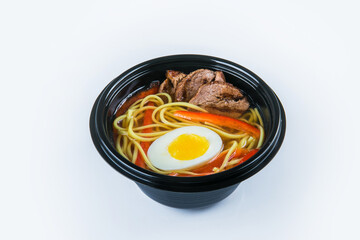Beef Udon Soup with egg, udon noodles and beef fillet, paprika (bell pepper) served in plastic delivery bowl. Dish isolated on gray background. Asian first dish in black plate. Food isolation