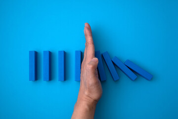 blue domino blocks that begins to fall and a hand that prevents it from falling.