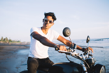 Fototapeta na wymiar Hispanic confident male sitting on motorbike on beach