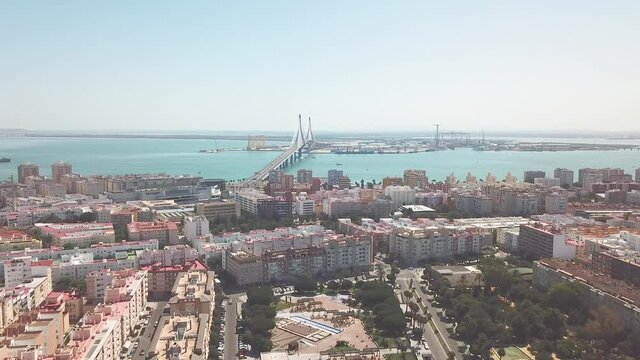 Cinematic generic aerial view of the commercial harbour of Cadiz. View of Bridge of Constitution 1812. Drone going forward. View of the Gardens of Varela - parck with the remains of ancient tombs. 