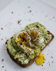 vegetarian toast with avocado and egg and spices on a white plate, close-up image with selected focus