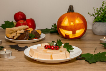 Next to the candles is a pumpkin with a carved face. Sweets for Halloween on the table.