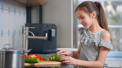 Cute schoolgirl cutting vegetables making salad for dinner