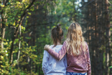 Fototapeta premium Two girls friends hugged and walk through the forest on a sunny day. Autumn coniferous forest in Siberia in Russia.