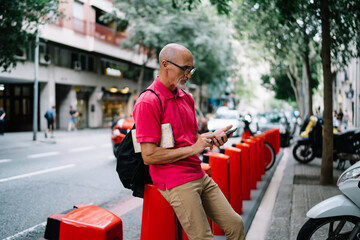 Aged male traveller using cellular device for reading informative publication and track location gps during getaway international trip, Caucasian man 60 years old messaging via mobile application