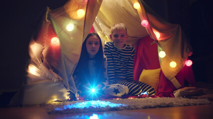 Brother and sister watching cartoons using projector sitting in wigwam © nimito