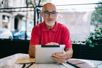 Man on retirement enjoying leisure in street cafe for messaging with old friends using modern touch pad for connecting to wireless internet, Caucasian male installing notification on digital gadget