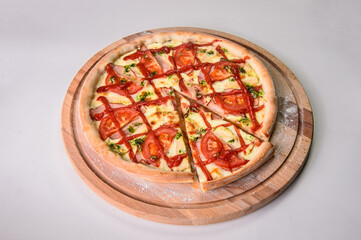 Whole uncut pizza on round wooden cutting board served with flour isolated on background. Restaurant fast food menu dish isolation. Slice of meat pizza with melted cheese, tomatoes and bbq sauce
