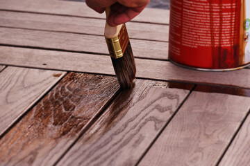 Male hand paints wood oil on thermo-ash with a broad brush, the paint bucket is in the background