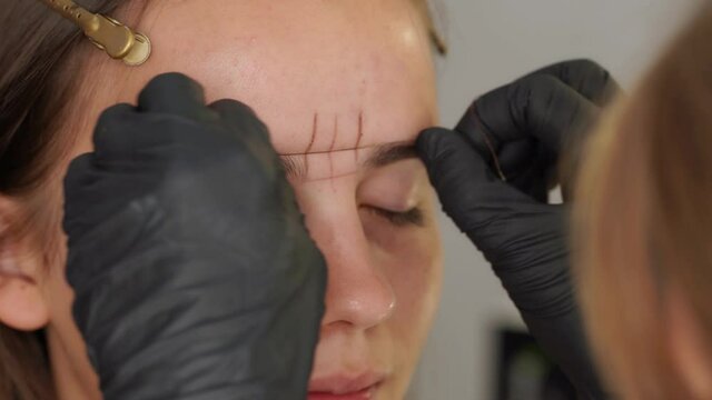 Professional styling, correction and shaping procedures of female eyebrows in beauty salon. Closeup view of client face and stylist's hands working with special thread to mark new contour of brows.