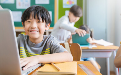 Portrait of Asian little boy using computer to learn lessons in elementary school. Student boy studying in primary. Children with gadgets. Education knowledge, technology internet network concept