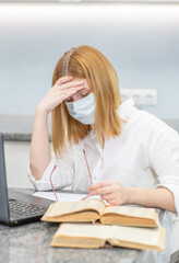 Tired teen girl with headache wearing medical mask sits at home. Distance learning. Quarantine and coronavirus epidemic concept