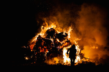 Hot red burning large fire with the black starry night sky. Silhouette of a fireman on the...