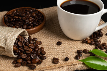 Coffee cup with beans on sackcloth and black background.