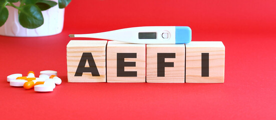 The word AEFI is made of wooden cubes on a red background with medical drugs. Medical concept.
