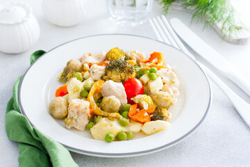 Baked vegetables - broccoli, brussels sprouts, bell peppers, peas, tomatoes, zucchini with chicken fillet, diet dish on a white table, selective focus