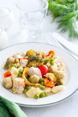 Baked vegetables - broccoli, brussels sprouts, bell peppers, peas, tomatoes, zucchini with chicken fillet, diet dish on a white table, selective focus