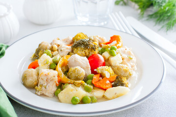 Baked vegetables - broccoli, brussels sprouts, bell peppers, peas, tomatoes, zucchini with chicken fillet, diet dish on a white table, selective focus