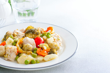 Baked vegetables - broccoli, Brussels sprouts, bell peppers, peas, tomatoes, zucchini with chicken fillet, diet dish on a white table, copy space