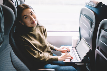 Fototapeta premium Satisfied young woman using laptop in train