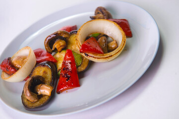 Side view of vegetarian dish. Mix of Grilled vegetables served on gray plate isolated on background. Grilled mushrooms, bell pepper, onion, zucchini and eggplant. Healthy food menu 
