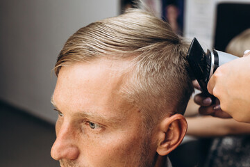 blonde man in barbershop. Haircut with an electric razor