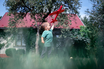 Happy kid playing with red airplane on lawn near his home