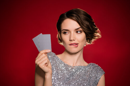 Closeup photo of attractive tricky lady professional casino player hold two cards risky gamer all in cheating bluffing bite lips wear shine dress isolated dark red gradient color background