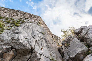 Bottom view of the rock and wall of a medieval fortress against a cloudy sky in Sibenik, Croatia