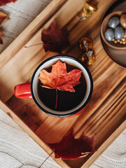 A red cup of tea is on a wooden tray on a knitted blanket. On a tray are sweets and dried oranges in chocolate. An autumn drink. A maple leaf floats in the cup. Mood autumn. Home comfort in the fall.