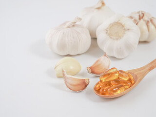 Capsule garlic oil in wooden spoon with fresh garlic on white background, the benefit of garlic is prevent the occurrence of heart disease