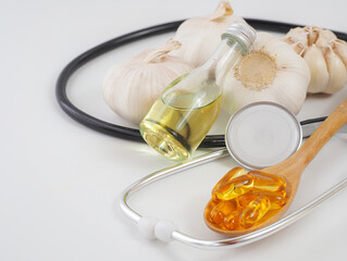 Capsule garlic oil in wooden spoon with garlic oil, stethoscope and fresh garlic background, the benefit of garlic