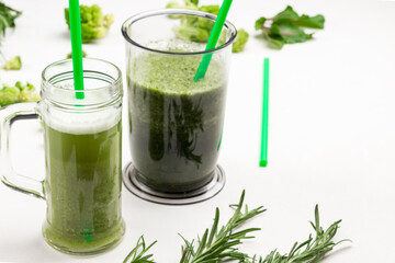 Mugs with green vegetable smoothies. Green straws in mugs. Sprigs of rosemary and broccoli on table.