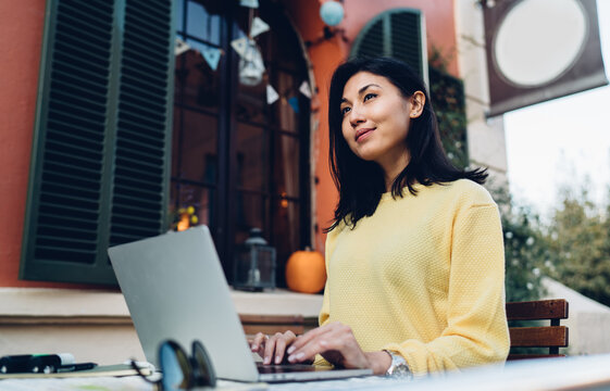 Pensive female student e learning in street cafeteria thoughtful looking away and thinking on projecting idea, Asian freelancer pondering on web design using laptop computer with 4g wireless internet