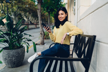 Happy Asian woman using smartphone on bench in town