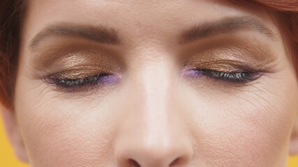 Close up of closed eyes with purple and gold eyeshadow of mature red hair woman. High quality photo